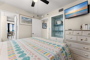 A bedroom with a bed, a dresser, a TV, and a door leading to a balcony. - Beachfront Gulf Views | Beach Chairs Service + Pools (Panama City Beach)