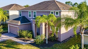 A single-story house with a dark roof, a garage, and a well-maintained lawn with palm trees. - Spacious 5 bedroom Florida villa (Davenport)