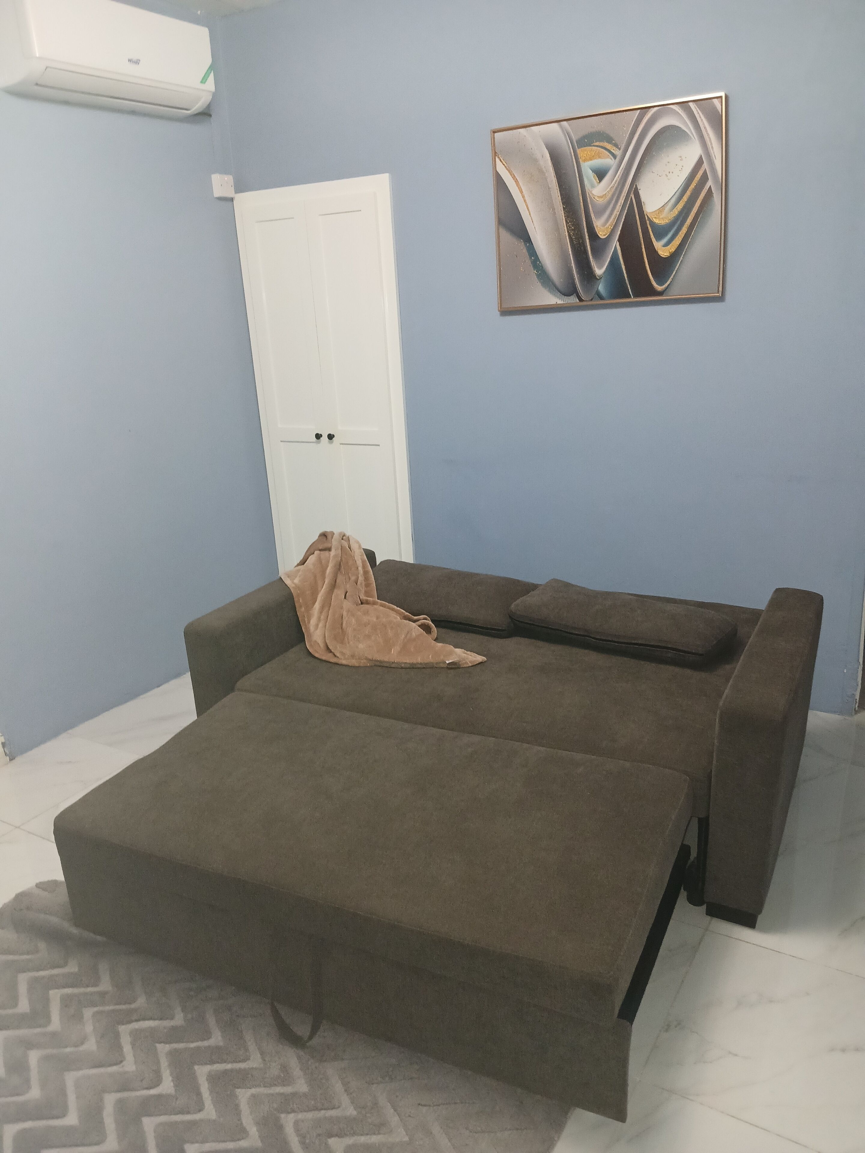 A room with a sofa bed, a door, and a wall-mounted abstract art piece.