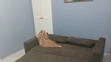 A room with a sofa bed, a door, and a wall-mounted abstract art piece.