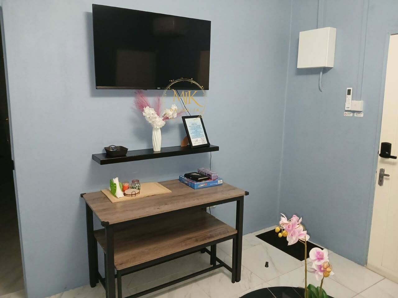 Une chambre dotée d’un téléviseur à écran plat fixé au mur, d’un bureau en bois orné d’un cadre photo, d’une petite étagère avec des objets décoratifs et d’une orchidée en pot.