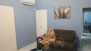 Ein Wohnzimmer mit einem braunen Sofa, einem schwarzen Couchtisch mit Topfpflanze, einer weißen Tür und einer Wand-Klimaanlage.