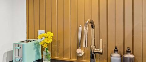 Eine Küche mit einem schwarzen Spülbecken, einem Toaster, einer Vase mit gelben Blumen, einem Wasserhahn und einer Wandleuchte.