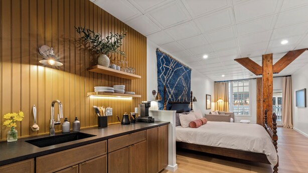 Ein modernes Schlafzimmer mit einem großen Bett, einem Holzkopfstück und Blick auf die Stadt durch große Fenster.