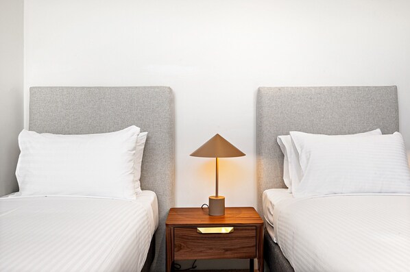 A hotel room with two beds, a nightstand with a lamp, and a plain white wall. - Stylish 3-bed Townhouse in Vibrant Fitzroy (Melbourne)