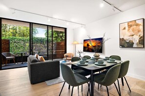 Uma sala de jantar moderna com uma mesa posta para quatro pessoas, rodeada por cadeiras estofadas verdes.
