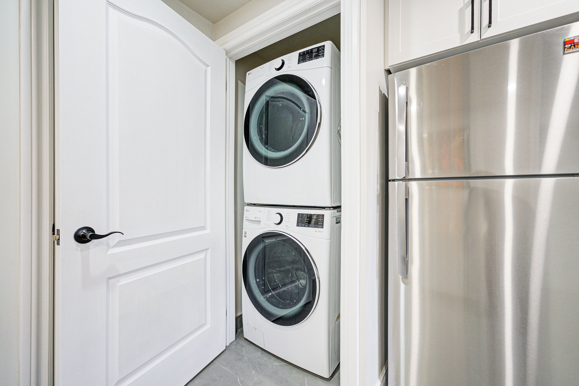 Un cuarto de lavado con dos lavadoras de carga frontal apiladas y un refrigerador de acero inoxidable.