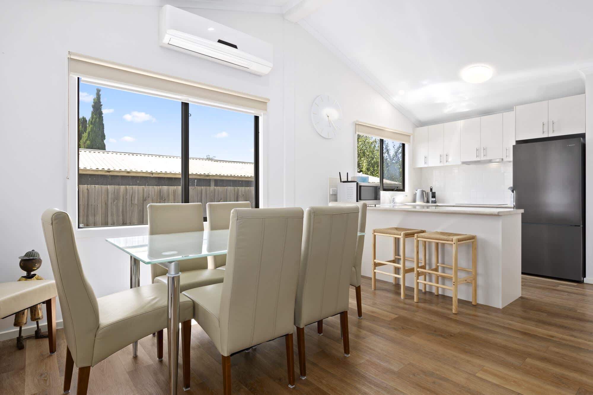 Une cuisine moderne avec des meubles blancs, un réfrigérateur noir et un coin repas comprenant une table et des chaises en verre.