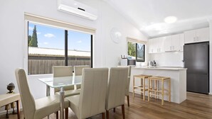 A modern kitchen with white cabinets, a black refrigerator, and a dining area with a glass table and chairs.