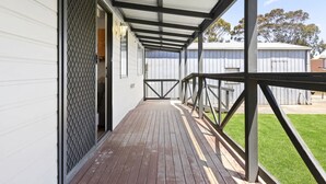 A covered outdoor area with a wooden deck, metal railing, and a view of a fenced yard.
