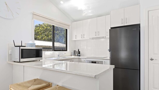 A modern kitchen with white cabinetry, a black refrigerator, a microwave, and a window overlooking greenery.