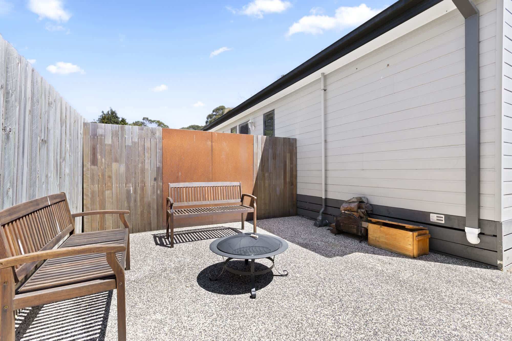 Ein Terrassenbereich im Freien mit einer Holzbank, einem runden Tisch und einem Kiesboden.