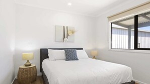 A neatly arranged bedroom with a bed, two bedside lamps, a decorative wall piece, and a window with blinds.
