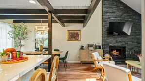 Un salon moderne doté d’une cheminée, de parquet et d’un coin repas avec une longue table et des chaises.