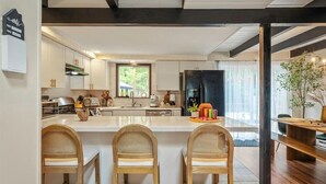 Une cuisine moderne avec des meubles blancs, un îlot central doté de tabourets et une grande fenêtre qui laisse entrer la lumière naturelle.