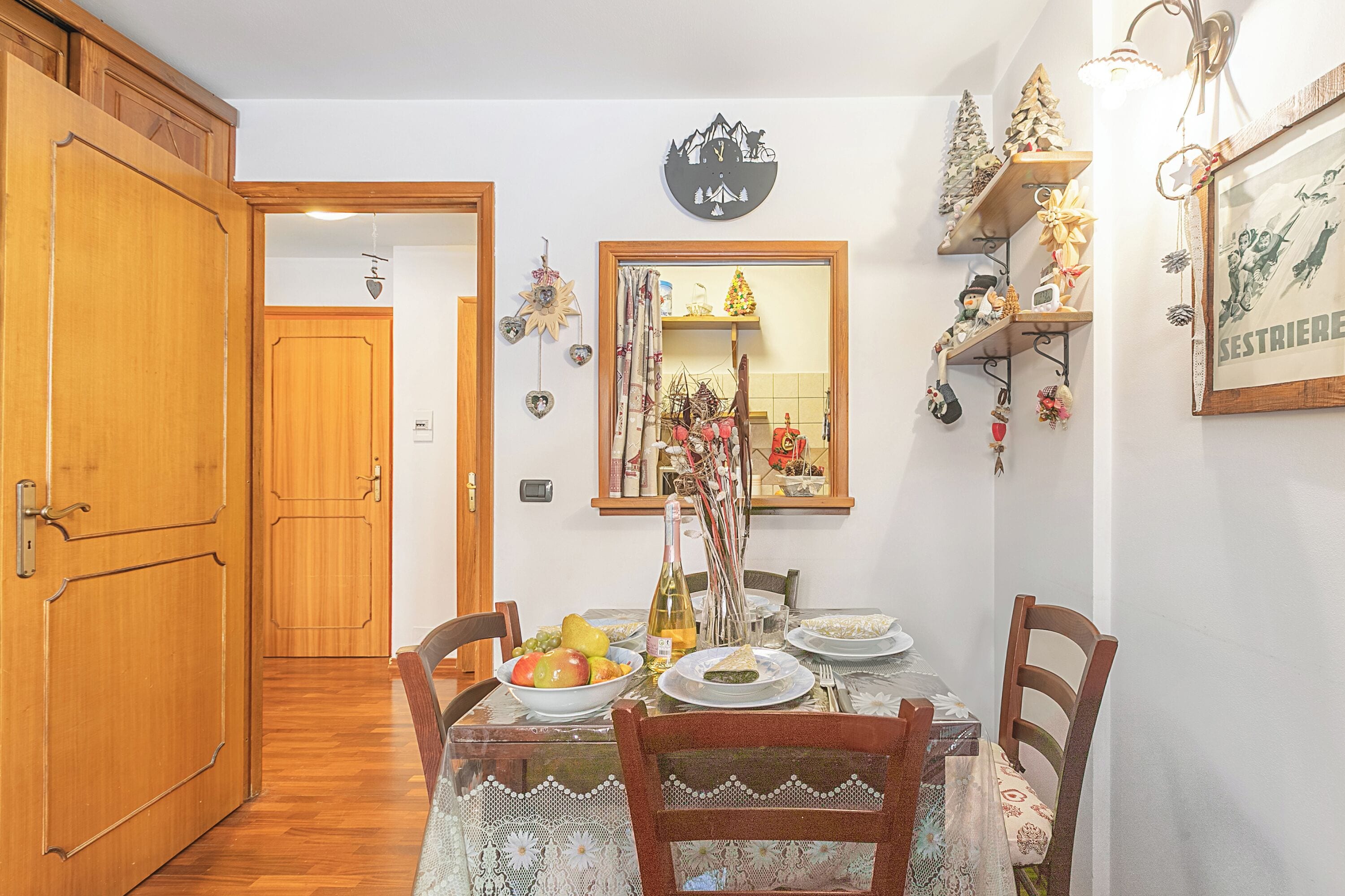 A dining area with a wooden table, chairs, and a mirror above. There are shelves with decorations and a framed picture on the wall.