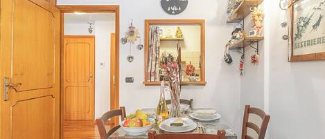 A dining area with a wooden table, chairs, and a mirror above. There are shelves with decorations and a framed picture on the wall.