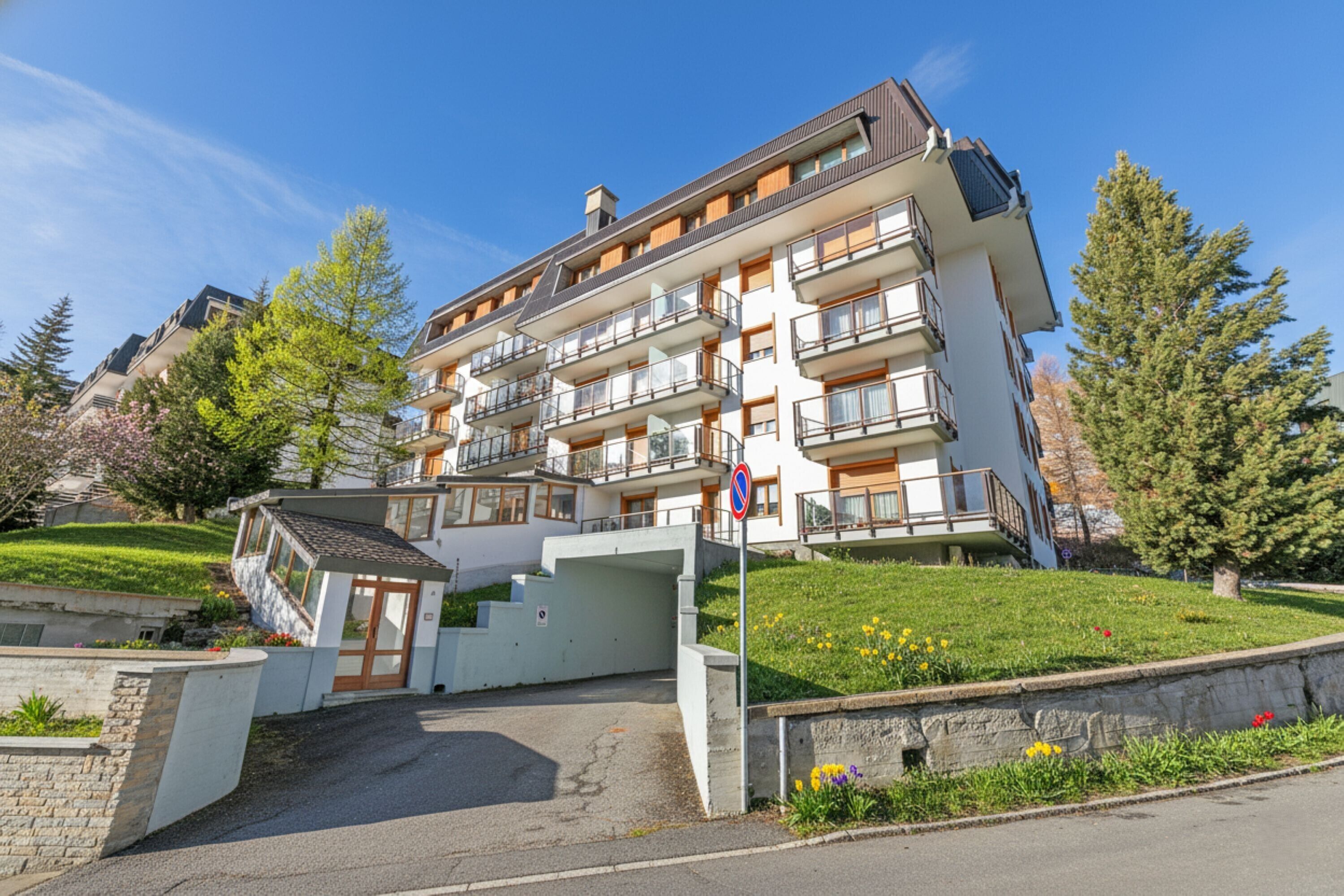 Un hotel a più piani con balconi, un'area di parcheggio e un piccolo edificio di ingresso.