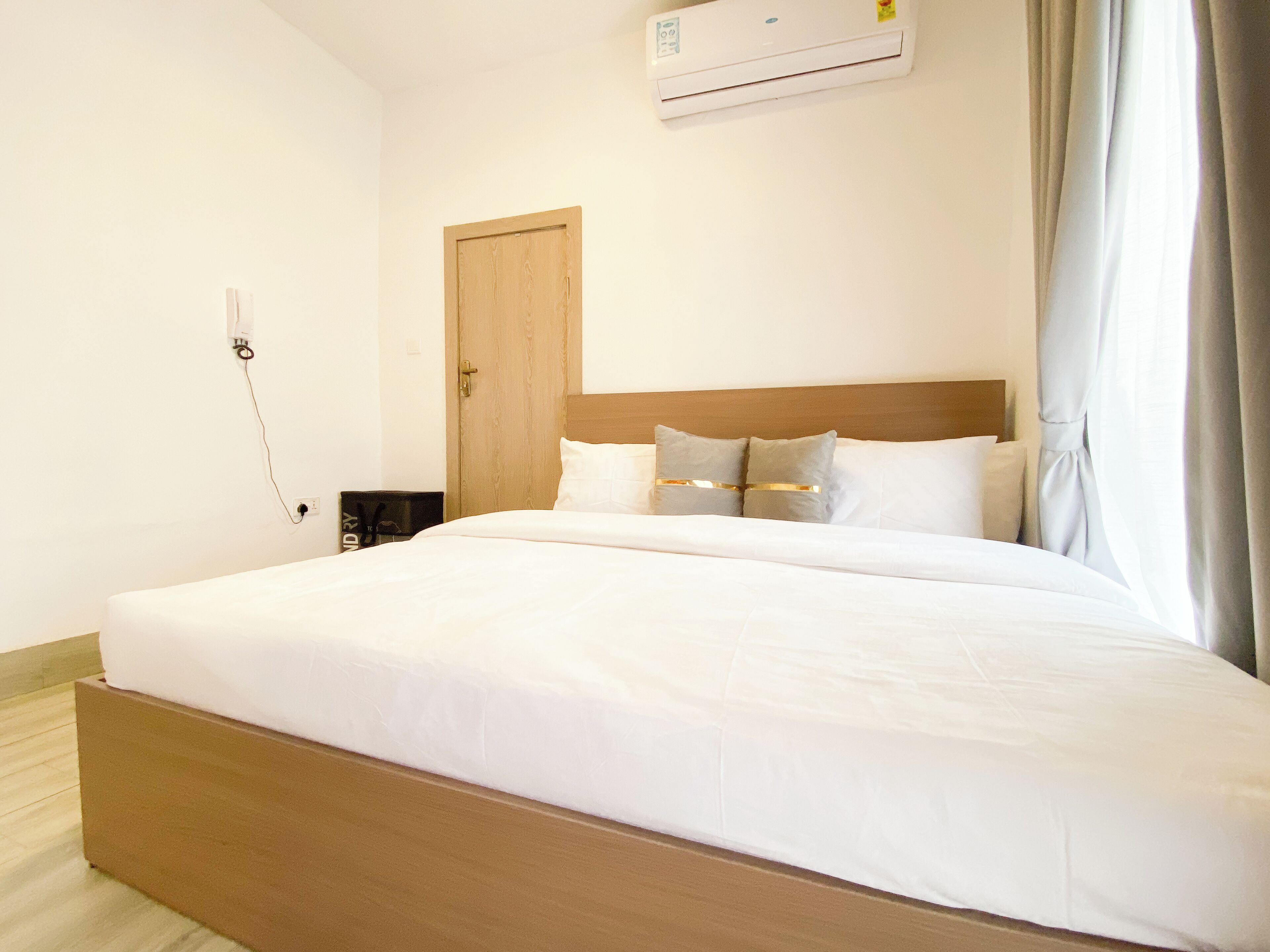 A hotel room with a bed, a wooden headboard, a wall-mounted air conditioner, and a door.