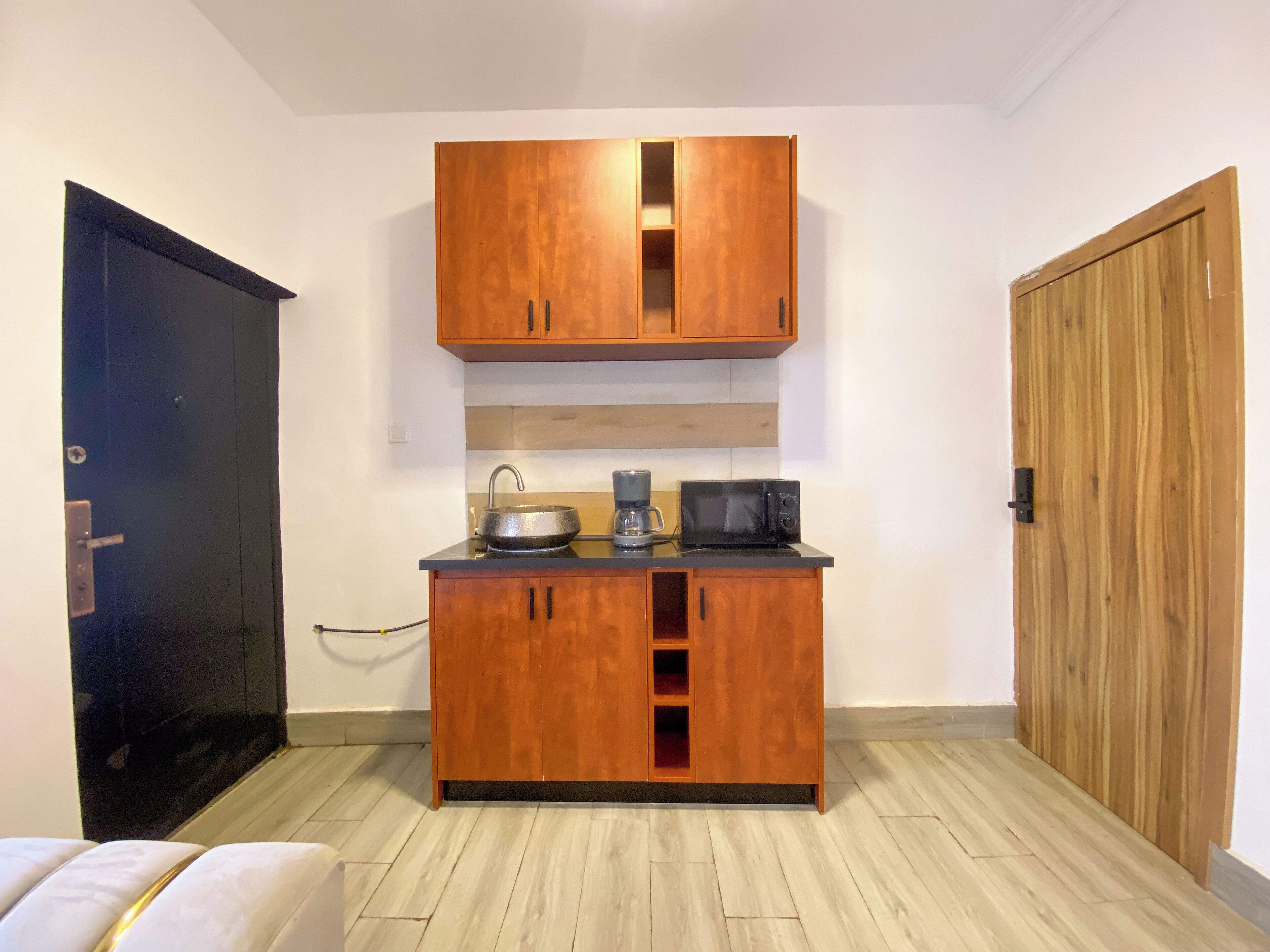 A compact kitchenette with a wooden cabinet, a sink, a coffee maker, and a microwave.