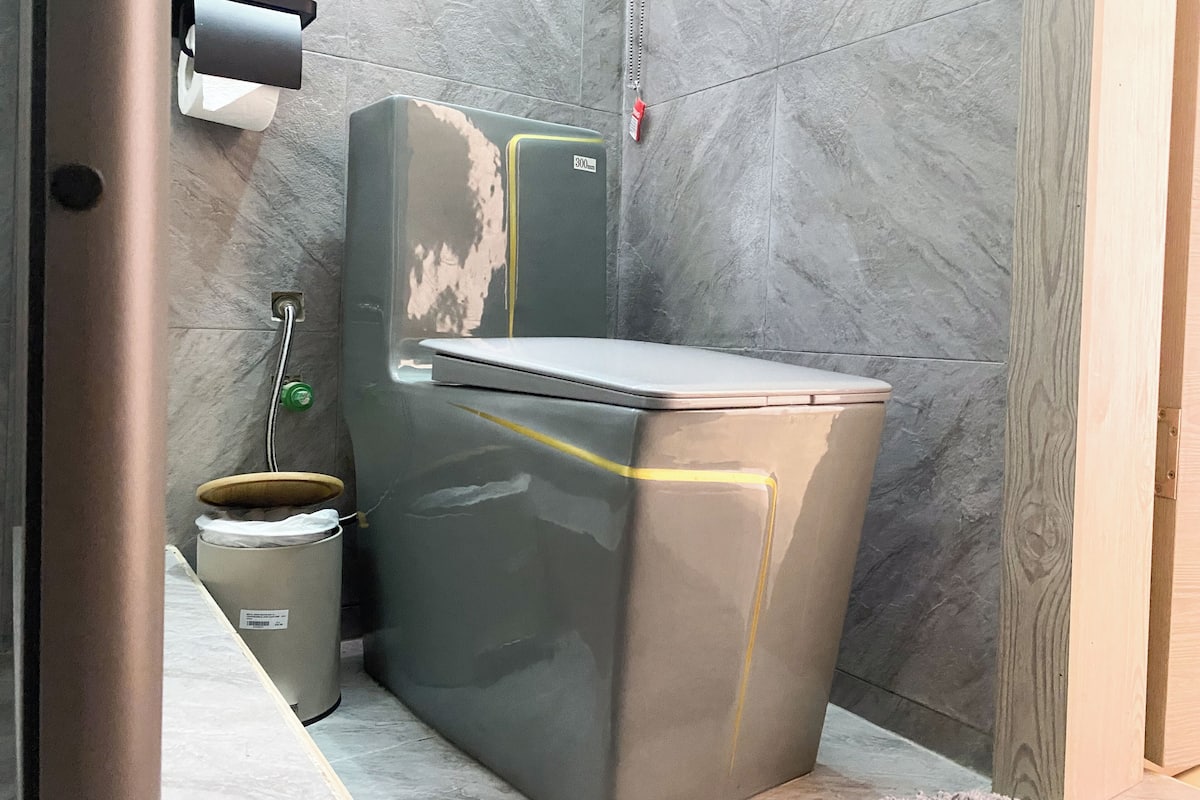 Ein kleines Badezimmer mit Toilette, einem Mülleimer und einem an der Wand montierten Händetrockner.