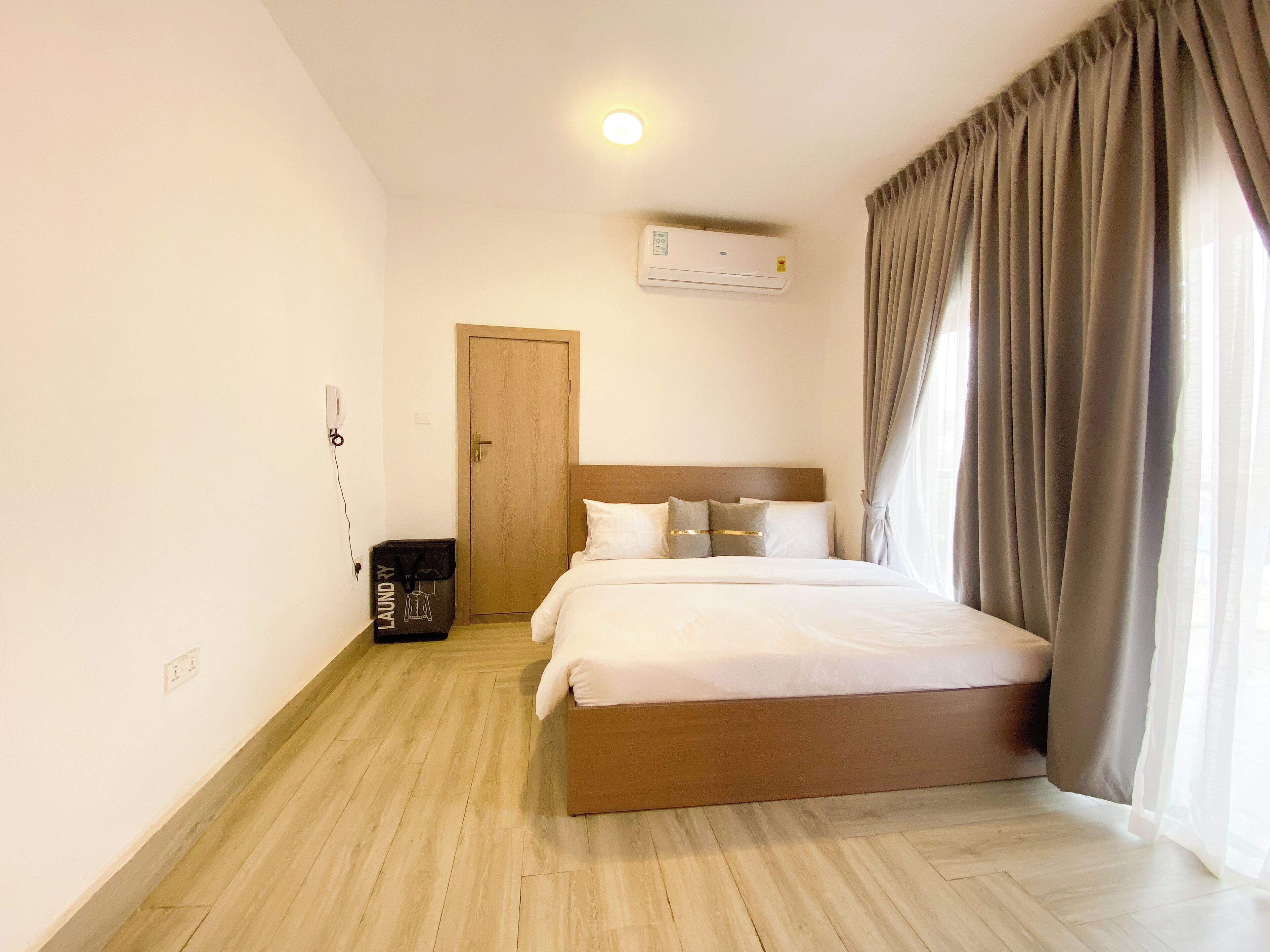 A hotel room with a wooden bed, a wardrobe, a door, and a ceiling-mounted air conditioner.