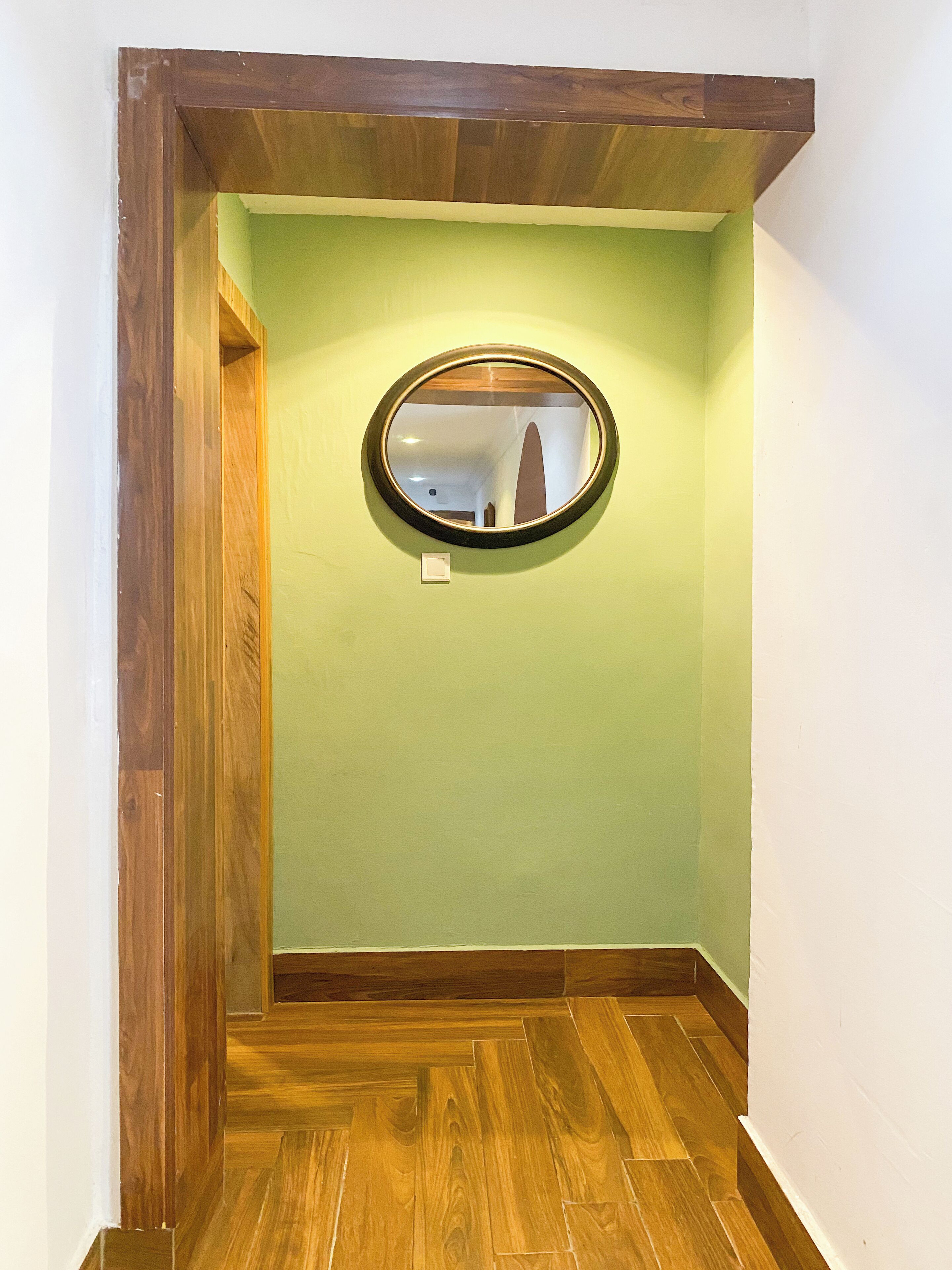 A hallway with a wooden floor, a green wall, and a round mirror on the wall.