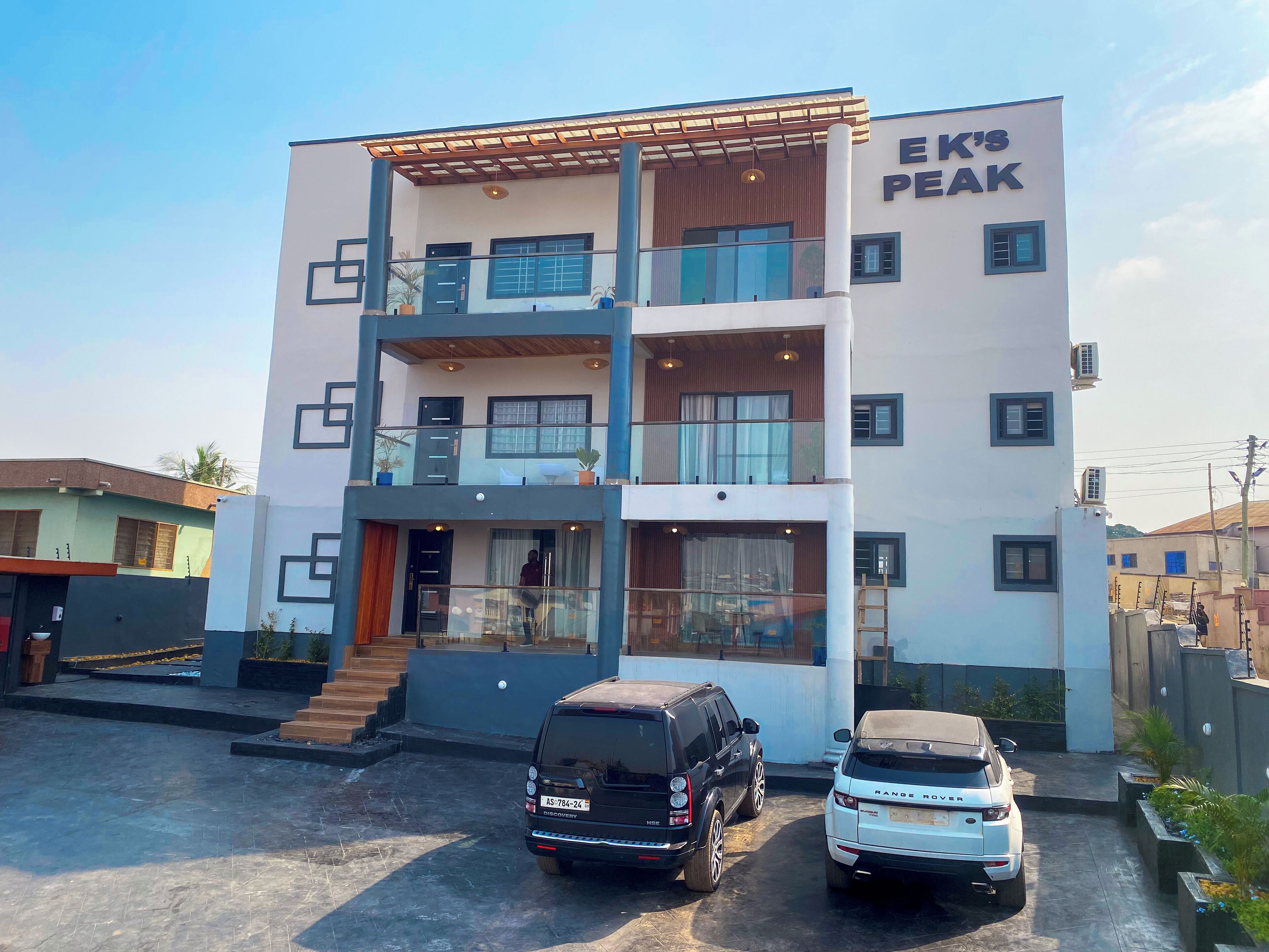 Un edificio de varios pisos con un letrero que dice "EK'S PEAK". Hay dos coches estacionados en la parte delantera.