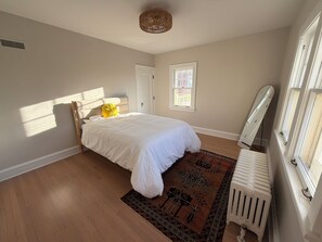 Ein Schlafzimmer mit Bett, Heizkörper, Fenster und Tür.