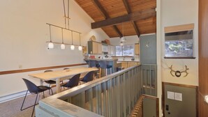 Cozinha moderna com vigas de madeira, luminárias pendentes e vista para o exterior através de uma janela.