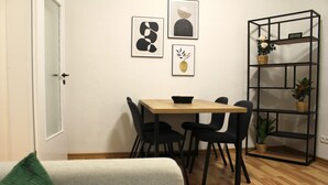 Un petit coin repas avec une table en bois et des chaises noires, une bibliothèque avec des plantes et des œuvres d’art encadrées accrochées au mur.