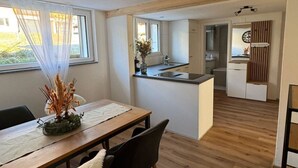 Una cocina moderna con una isla central, un comedor con mesa y sillas de madera, y vistas al área de estar a través de un arco abierto.