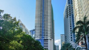 A tall, modern high-rise building with a distinctive blue and white facade, surrounded by other high-rise buildings and lush greenery. - Brickell Bay 2308 (Miami)