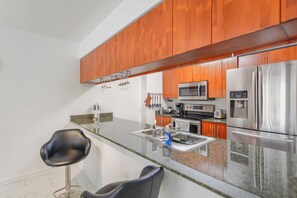 A modern kitchen with wooden cabinets, stainless steel appliances, granite countertops, and two black bar stools. - Brickell Bay 2308 (Miami)