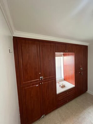 A room with a large wooden wardrobe, a small window with blinds, and a tiled floor. - 2BR/1B - Sunny Hollywood Hideaway (Hollywood)