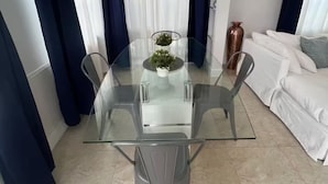 A modern dining area with a glass table and chairs, a potted plant, and a white sofa in the background. - 2BR/1B - Sunny Hollywood Hideaway (Hollywood)
