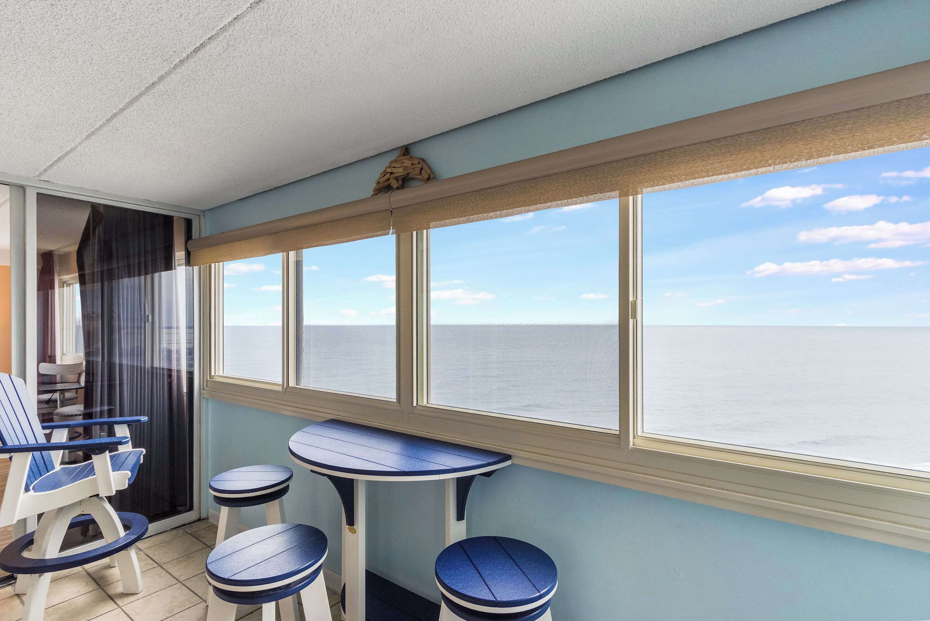 A balcony with a view of the sea, a table, two chairs, and a small stool.