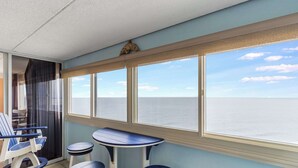 Un balcone con vista sul mare, un tavolo, due sedie e uno sgabello.