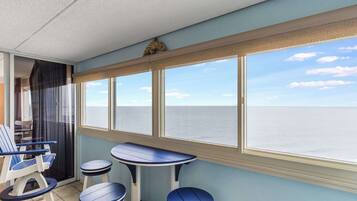 A balcony with a view of the sea, a table, two chairs, and a small stool.