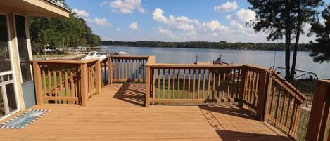 A wooden deck with railings, a view of a lake, and boats in the background.