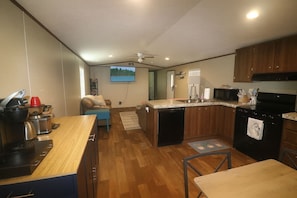 Eine kompakte Küche mit Geschirrspüler, Mikrowelle und Herd. Es gibt einen kleinen Essbereich mit Tisch und Stühlen. Ein Deckenventilator ist sichtbar, und ein Fernseher ist an der Wand montiert.