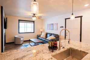 A modern kitchen with a marble countertop, a built-in sink, and a ceiling fan. There is a dining area with a table and chairs, and a living room with a sofa and a window. - Sleeps 30+, Boat Launch, 35 minutes to Yellowstone (Island Park)