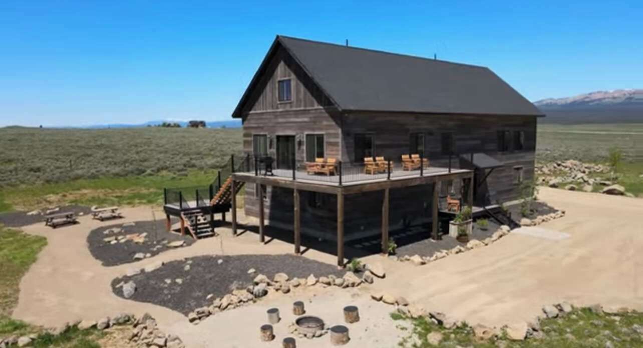 A rustic cabin with a large deck, surrounded by a natural landscape.