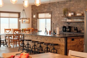 A modern kitchen with a central island, bar stools, wooden chairs, and a brick wall. - Sleeps 30+, Boat Launch, 35 minutes to Yellowstone (Island Park)