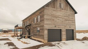 Ett tvåvåningshus i trä med en balkong, ett garage och utsikt över ett snötäckt landskap.