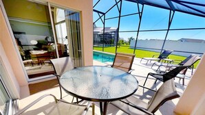Een glazen balkon met uitzicht op een zwembad, buitenzitplaatsen en een glazen tafel.
