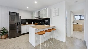 A modern kitchen with white cabinetry, a stainless steel refrigerator, a wooden island with bar stools, and a black stove. - Spacious 1-bed Apartment in Coolangatta (Gold Coast)