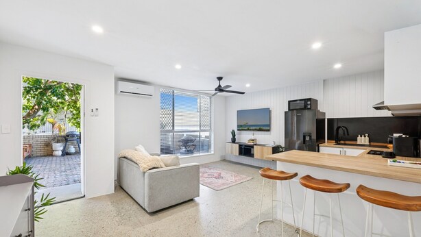 A modern kitchen with a bar area, a grey sofa, and a ceiling fan. - Spacious 1-bed Apartment in Coolangatta (Gold Coast)