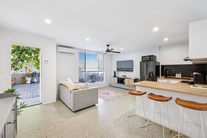 A modern kitchen with a bar area, a grey sofa, and a ceiling fan. - Spacious 1-bed Apartment in Coolangatta (Gold Coast)