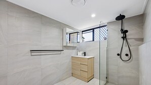 A modern bathroom with a glass-enclosed shower, a wooden vanity, and a small window with a view. - Spacious 1-bed Apartment in Coolangatta (Gold Coast)